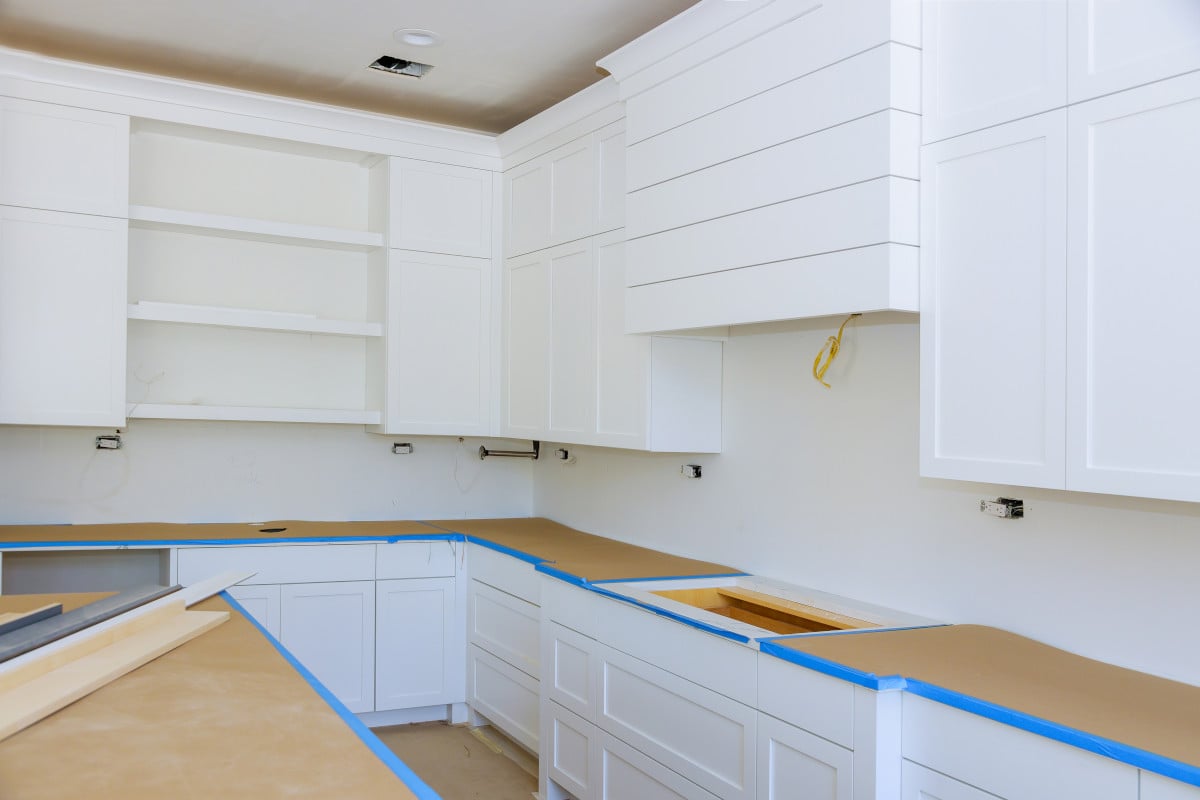 Kitchen renovation in progress with cabinets primed and surfaces protected for painting