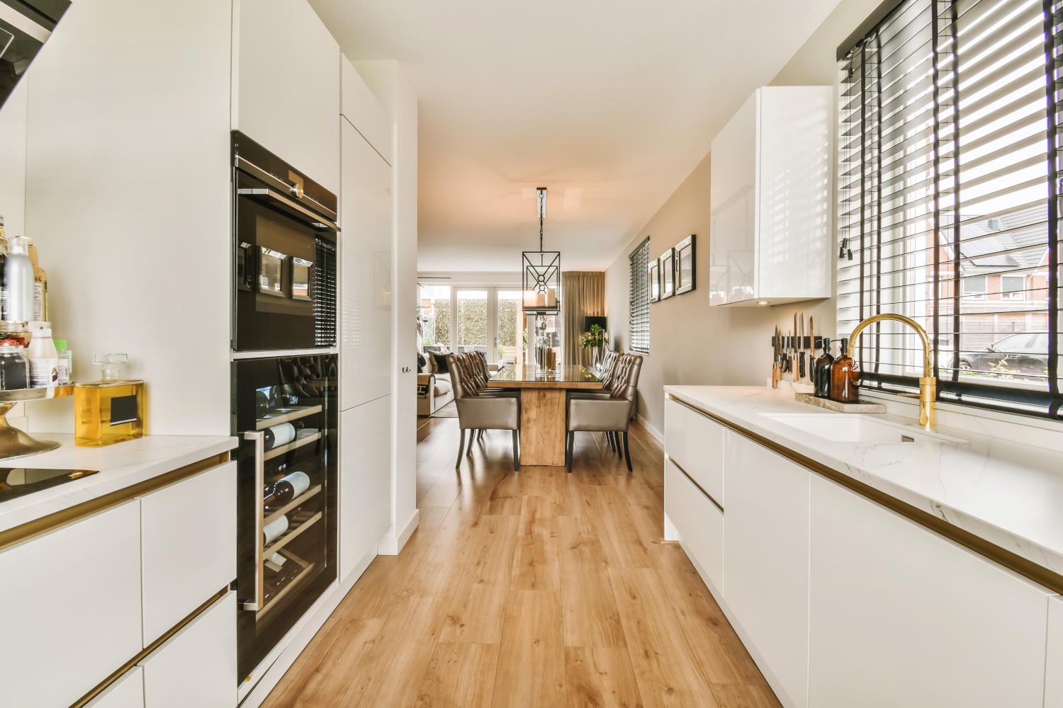 Modern galley kitchen featuring white cabinets, tall built-in appliances, and a gold faucet with wood flooring – perfect example of a space-saving layout.