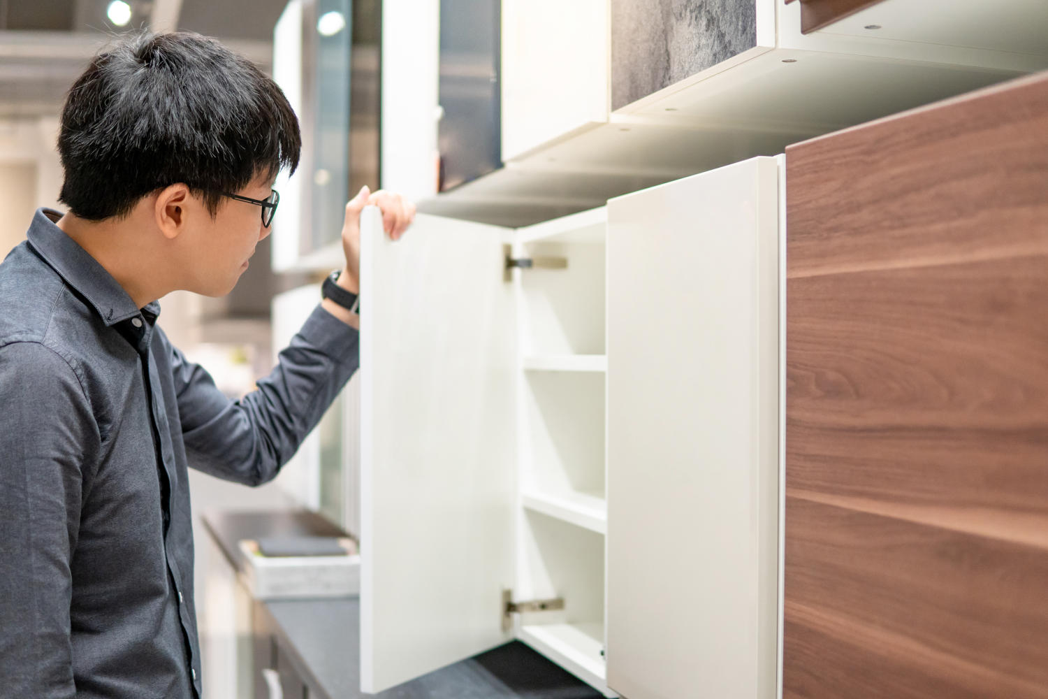 Person examining modern white base cabinet with adjustable shelves in a showroom, comparing shallow and standard cabinet depth options.