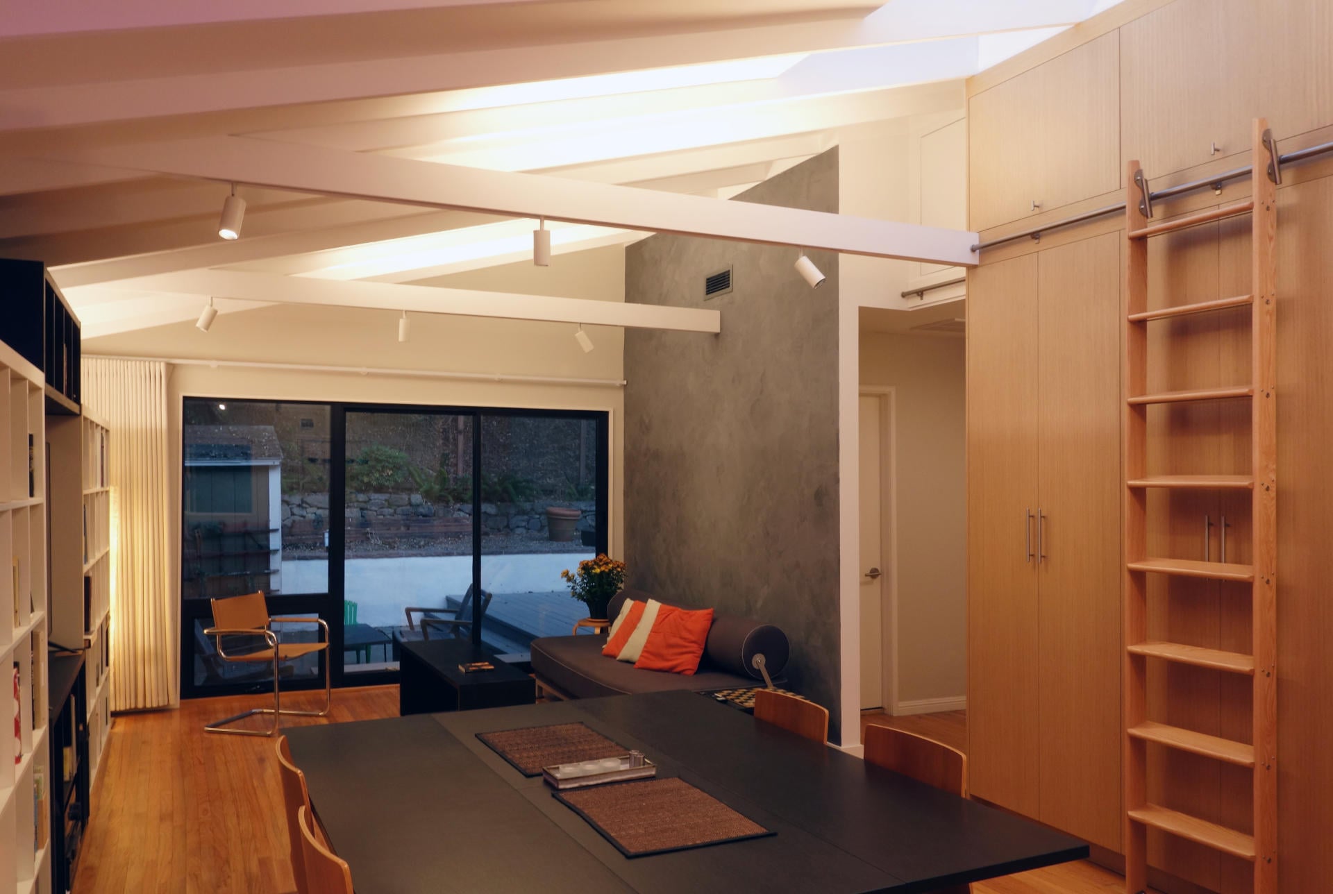 Light oak veneer cabinet wall with rolling ladder in mid century modern great room at dusk