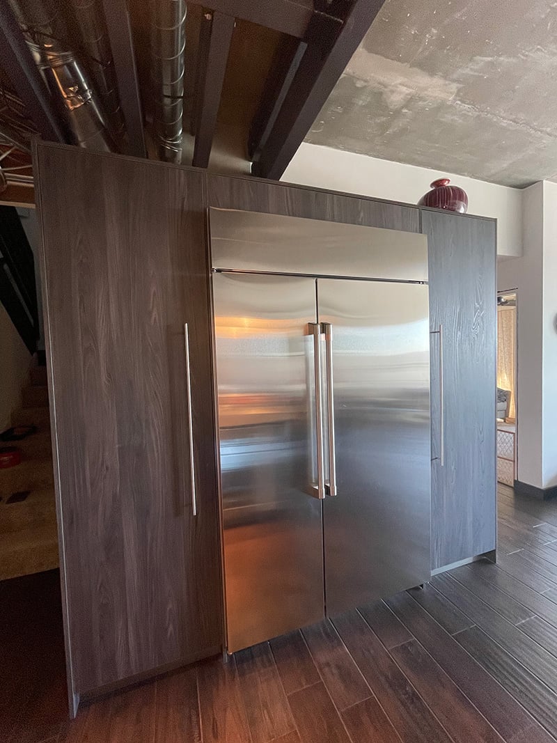 Tall kitchen cabinets surrounding a modern stainless steel refrigerator